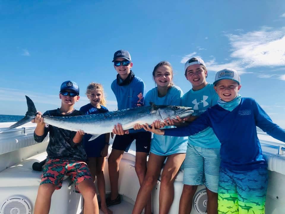Young anglers holding a large Kingfish on the boat